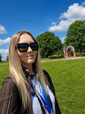 Magdalena Miller, przewodnik PTTK po Gietrzwałdzie dla pielgrzymek i grup parafialnych, na tle stacji drogi krzyżowej w Gietrzwałdzie.