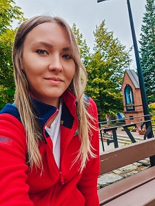 Magdalena Miller, przewodnik po Gietrzwałdzie, przy Kapliczce Objawień, w bluzie z napisem ‘Przewodnik’ i logo Koła Przewodników PTTK Olsztyn.